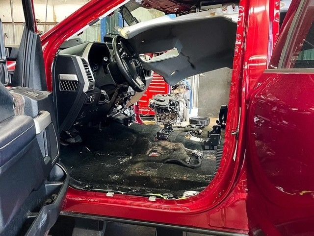 Red car interior heavily damaged after a fire, with burned floor and exposed seats.