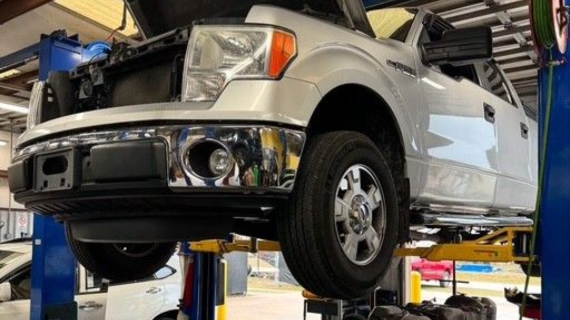 Silver pickup truck on a lift in an auto repair shop, viewed from the front-left side