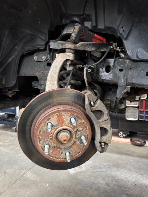 Car wheel removed, exposing brake rotor, caliper, and suspension inside a garage.
