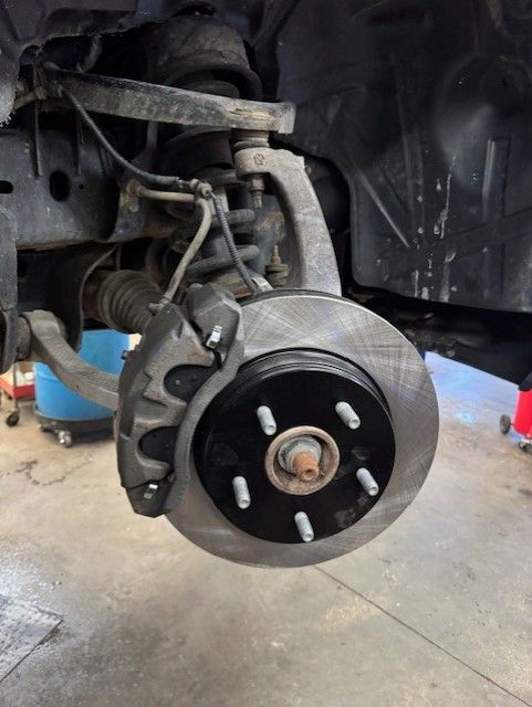 Car brake rotor and caliper with wheel removed in a garage, showing the suspension assembly