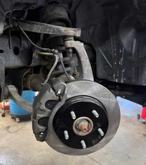 Front vehicle suspension assembly, including a brake rotor, caliper, and suspension components, in a garage setting.