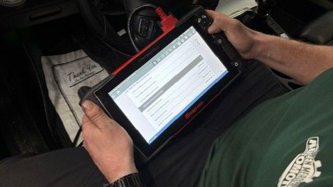 Person holding a tablet displaying a form inside a vehicle interior.
