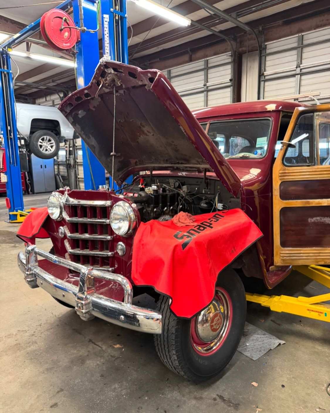 Red vintage truck with hood open in an auto shop, showing engine and chrome grille.