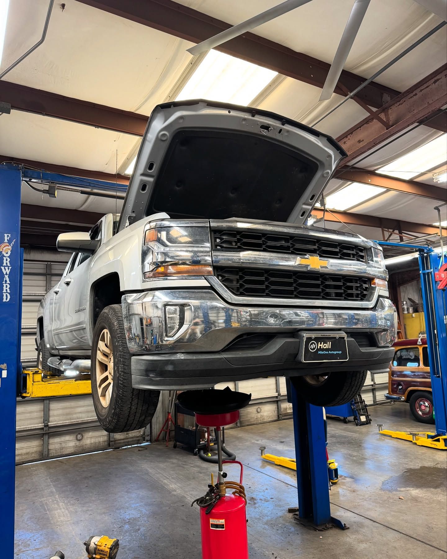 White pickup truck raised on a lift in an auto repair shop, hood open during maintenance.