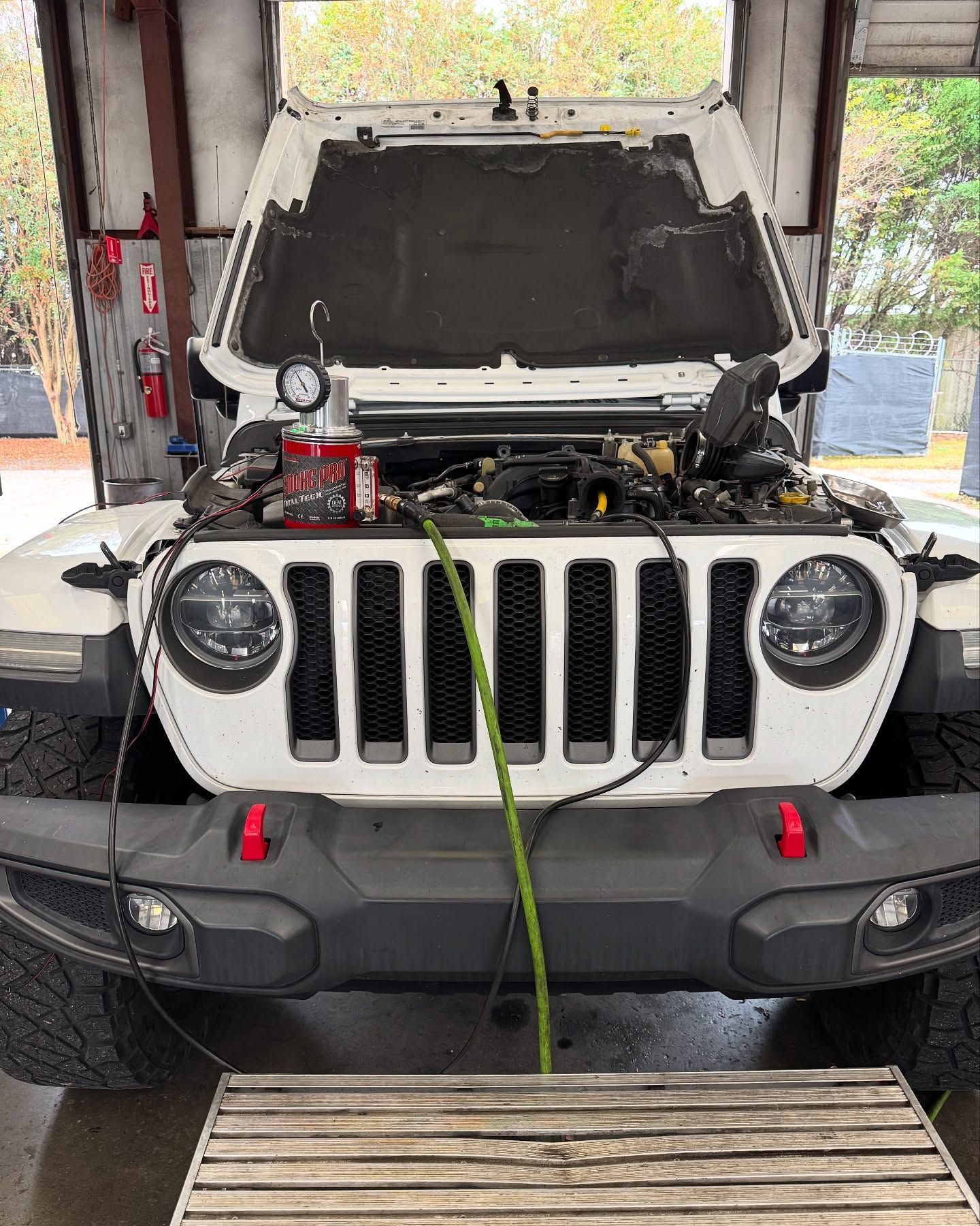 White Jeep in a garage with hood open and a green strap hanging from the front.