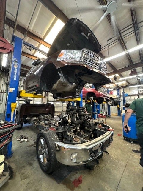 Car lifted on a shop hoist above a partly disassembled vehicle in an auto repair garage.