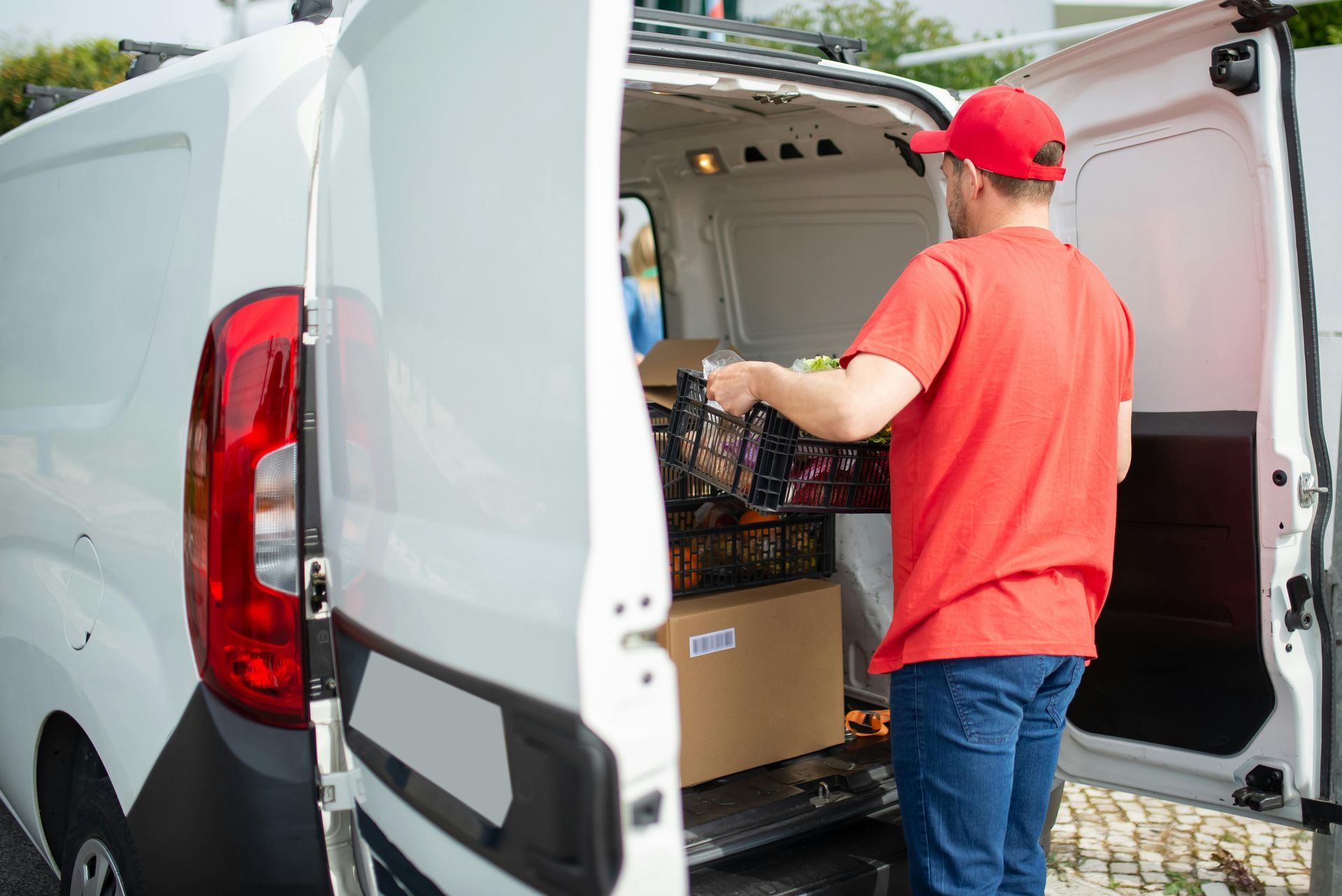 Person in red shirt loading crates into white delivery van outdoors in Wilmington NC.