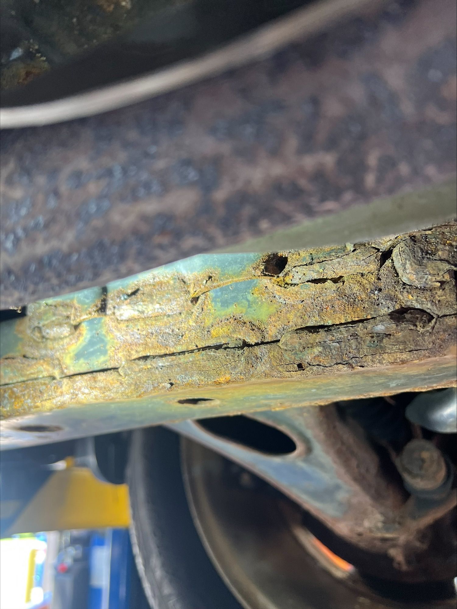 Close-up of a rusted, peeling metal car part with corrosion and chipped paint