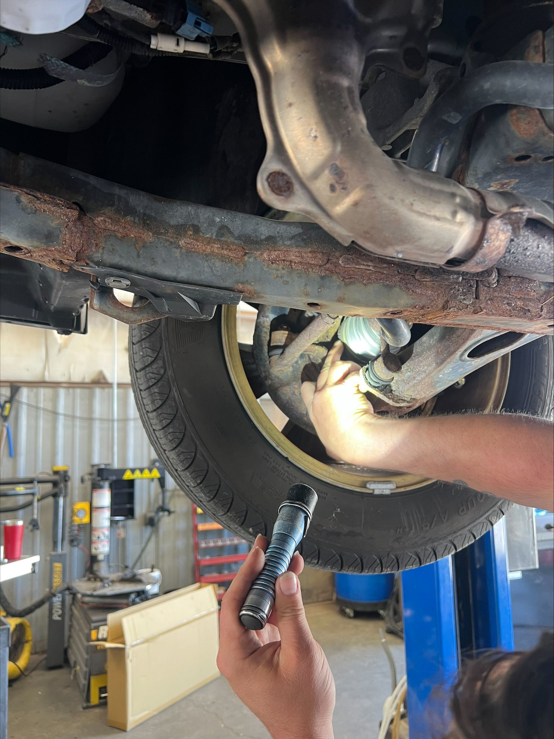Mechanic inspecting a car’s undercarriage with a flashlight in a garage lift area