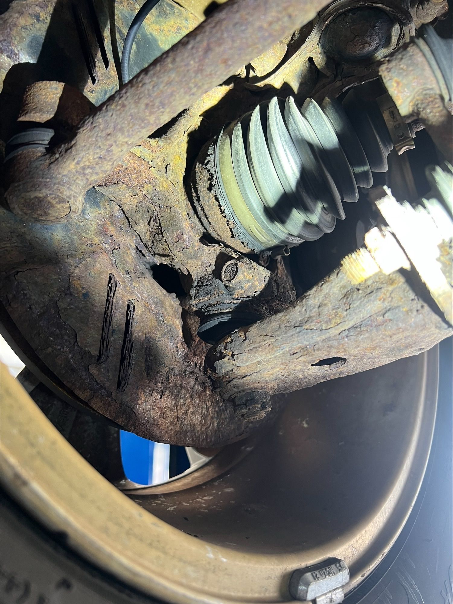 Close-up of a damaged car axle joint with torn CV boot and exposed grease inside a wheel well