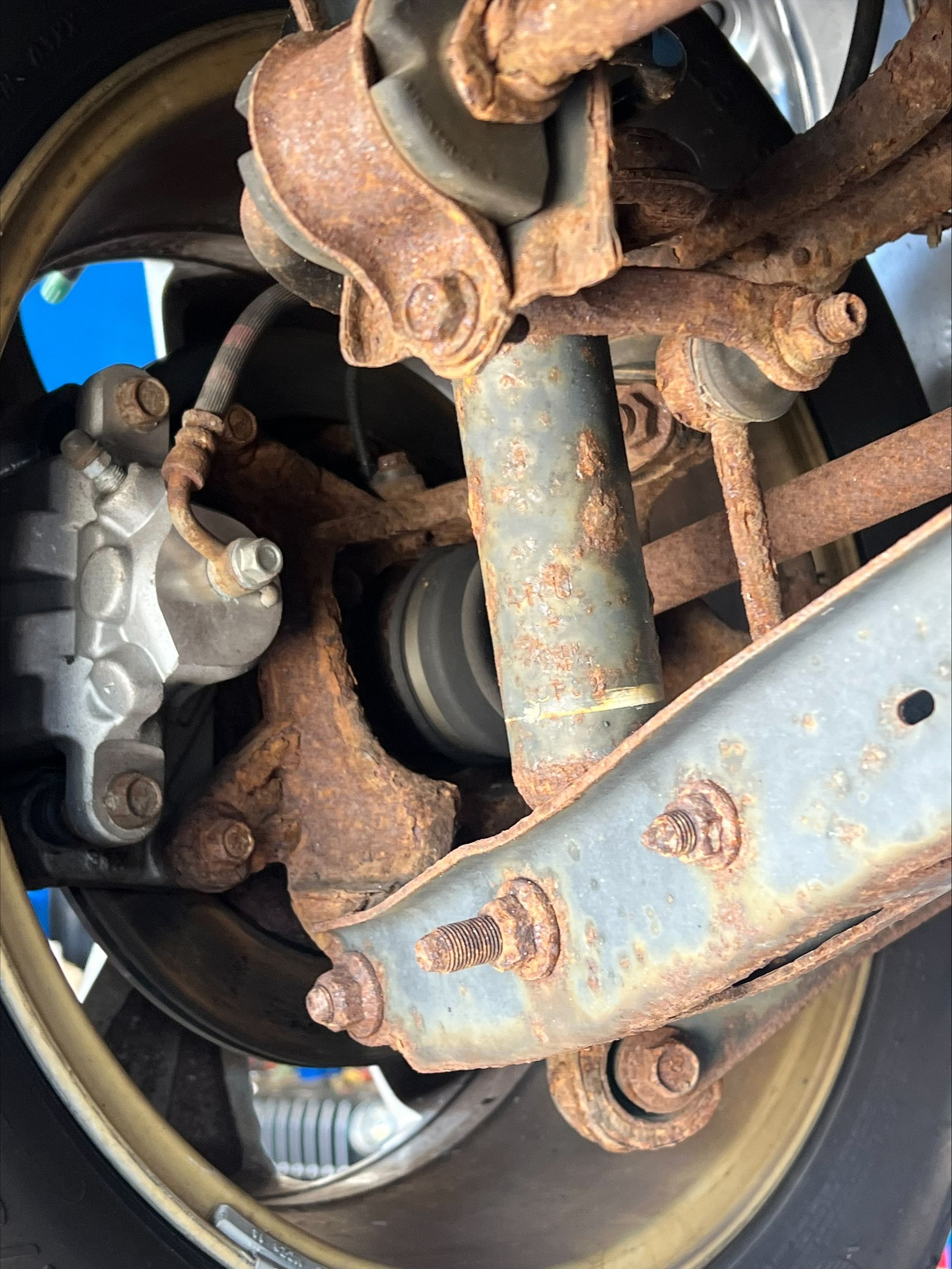 Rusty car wheel, suspension, and brake components in close-up view.