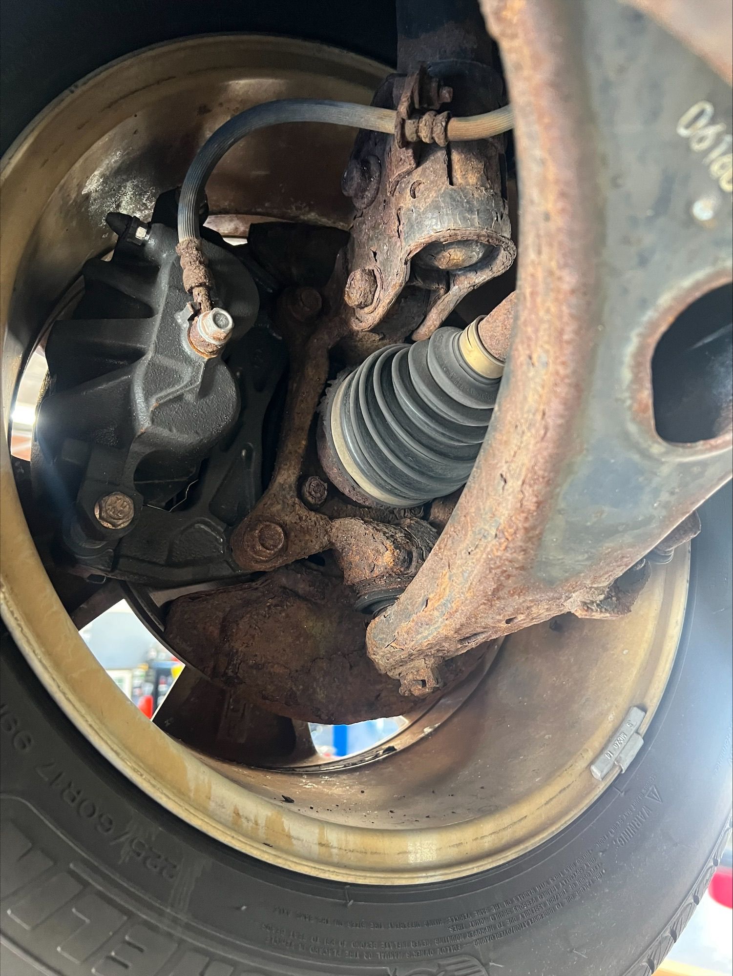 Close-up of a car wheel well showing suspension, brake parts, and an axle boot with rust on the metal components