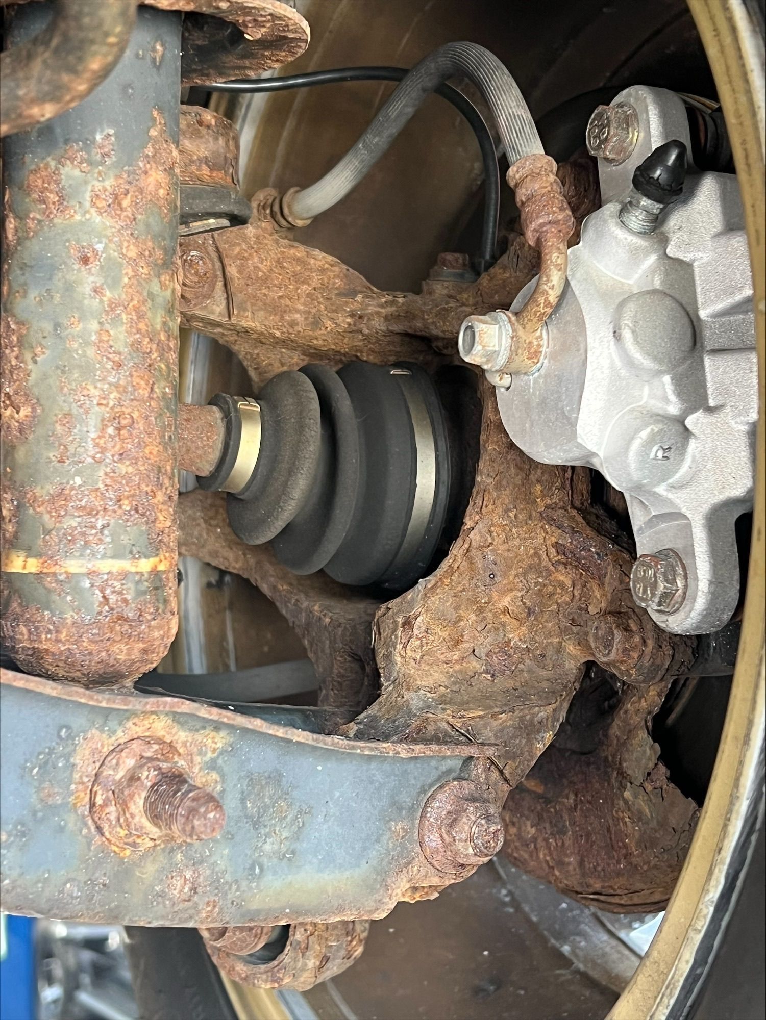 Rusty car suspension with exposed CV axle boot and silver brake caliper.