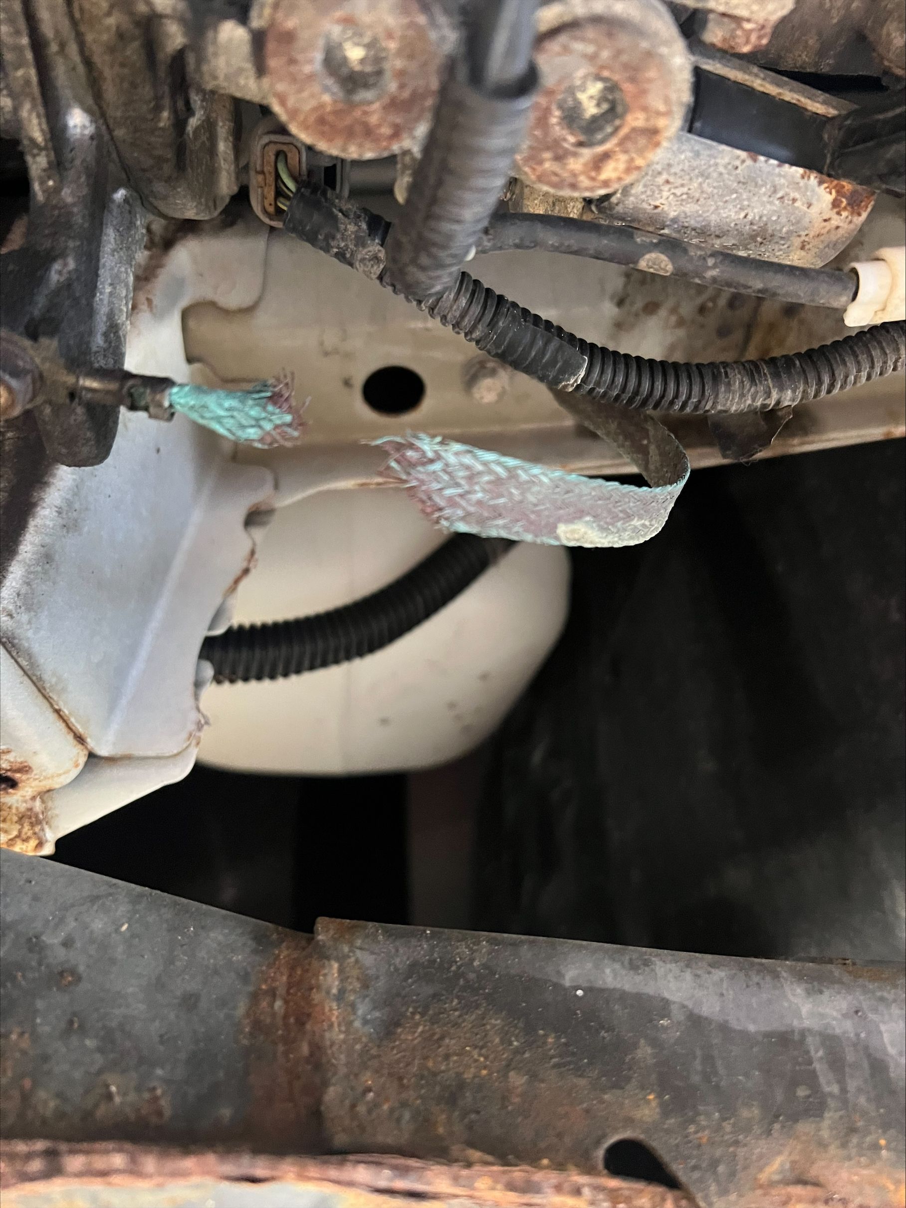 Close-up of a corroded metal bracket with wiring and a white circular component behind it
