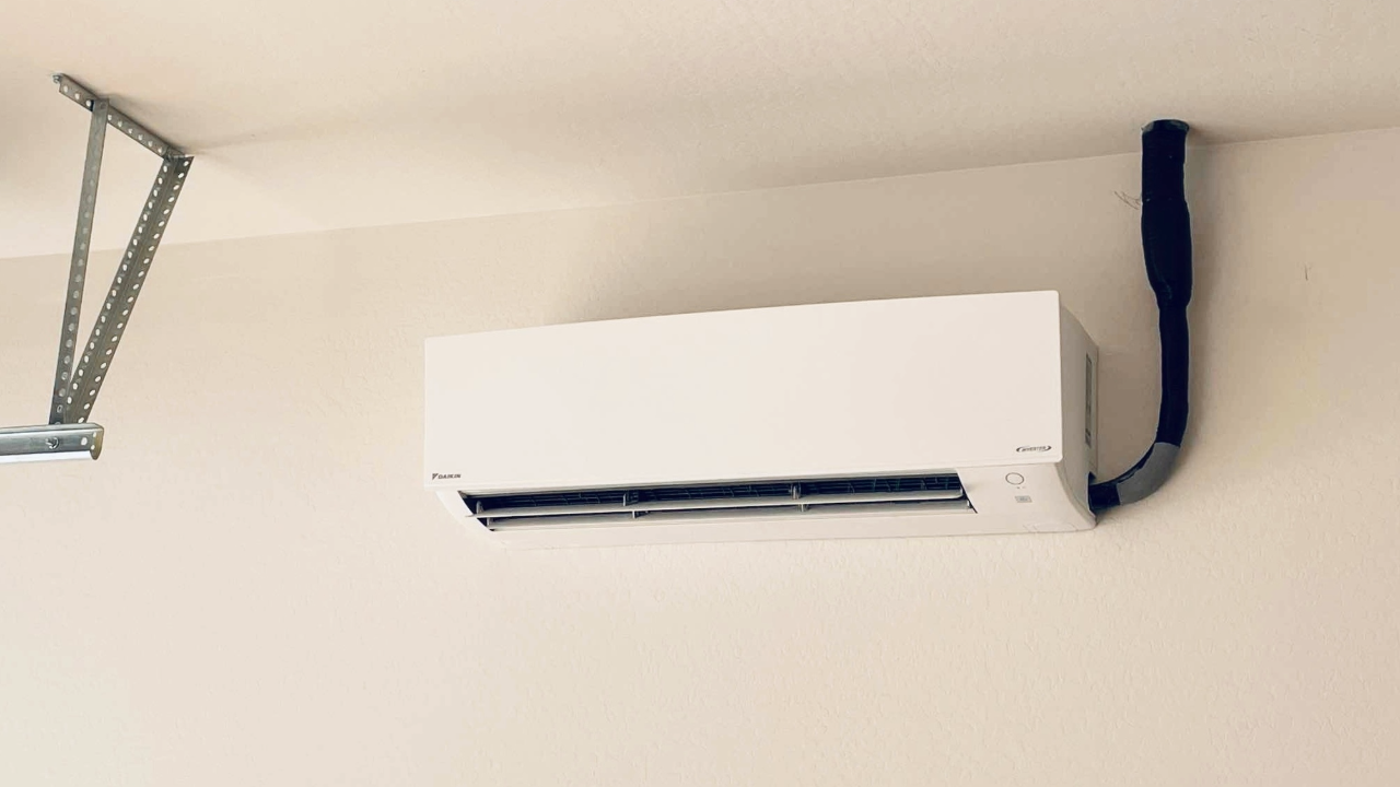 A white air conditioner is hanging from the ceiling in a garage.