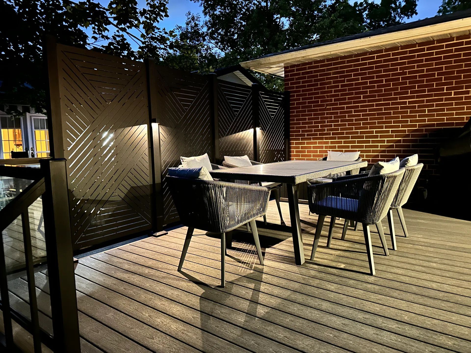 Outdoor patio with dining table, black chairs, and a brick wall in warm evening light
