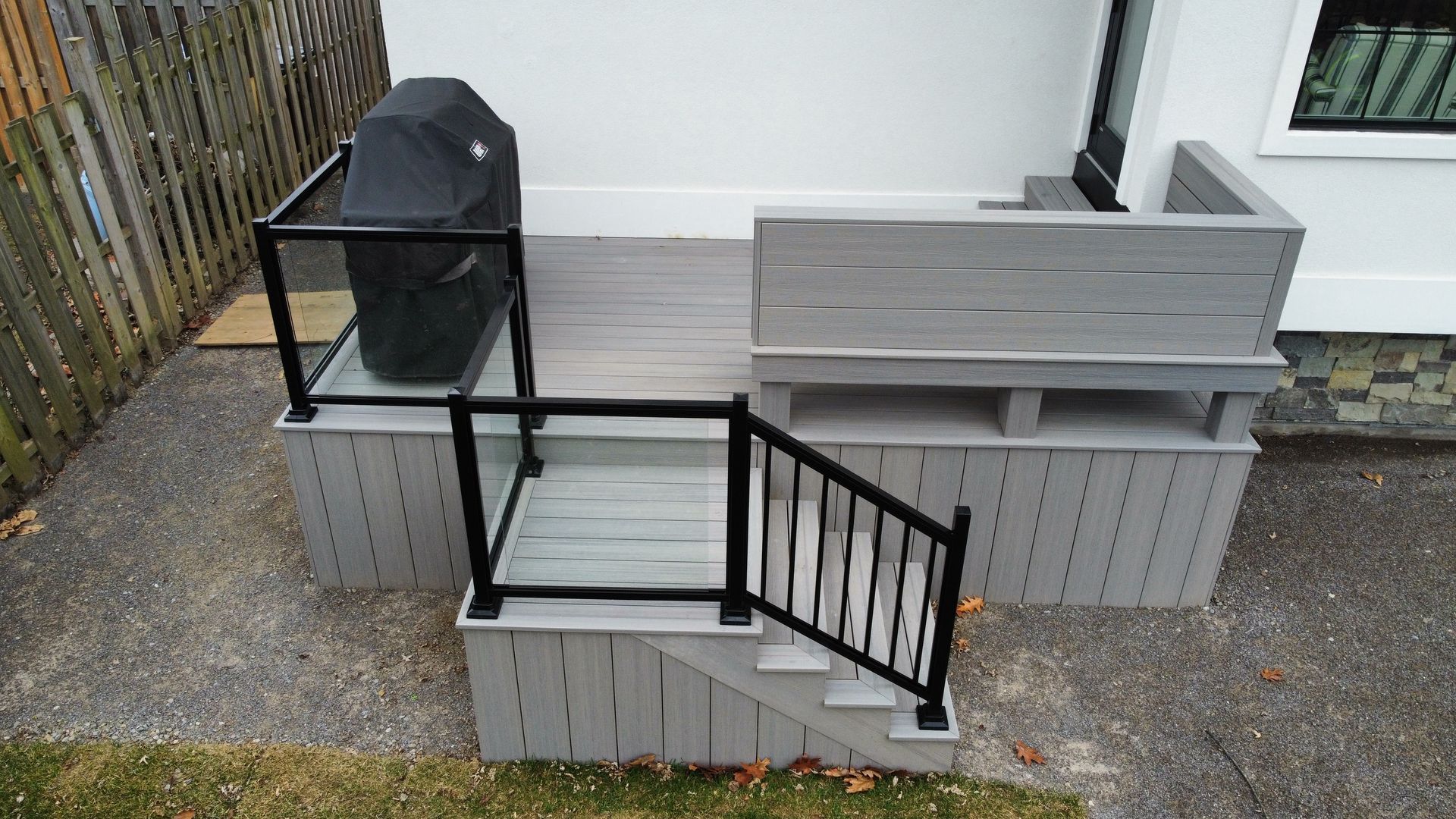 Small outdoor patio with gray brick planters, black metal railing, and a storage bin beside steps.
