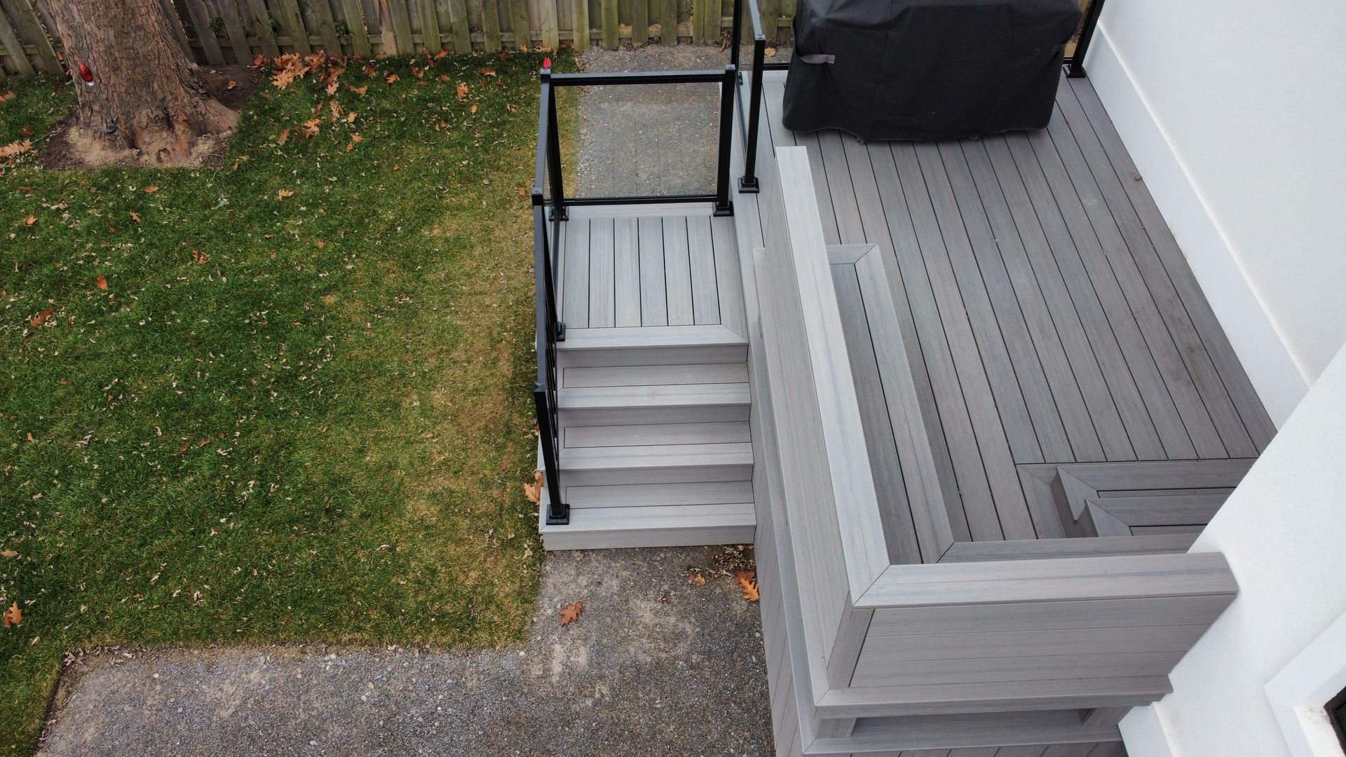A high-angle view of a grey deck with stairs leading down to a stone walkway and green grass in a backyard.