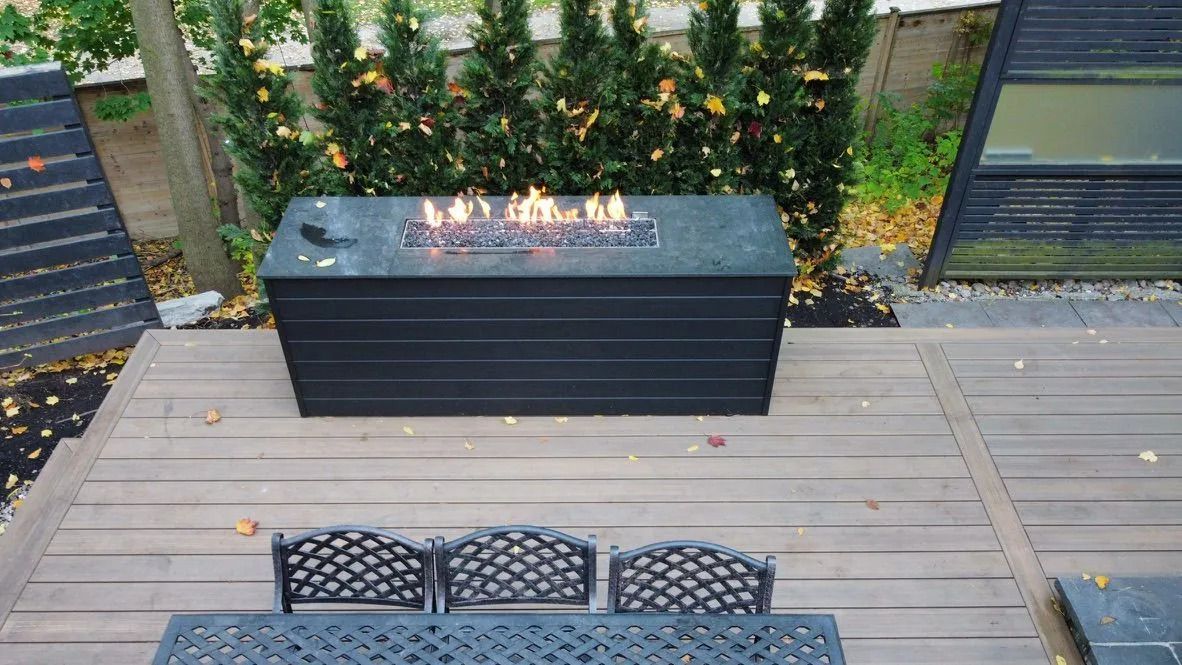 Backyard deck with a black fire table, greenery wall, and patio chairs in the foreground