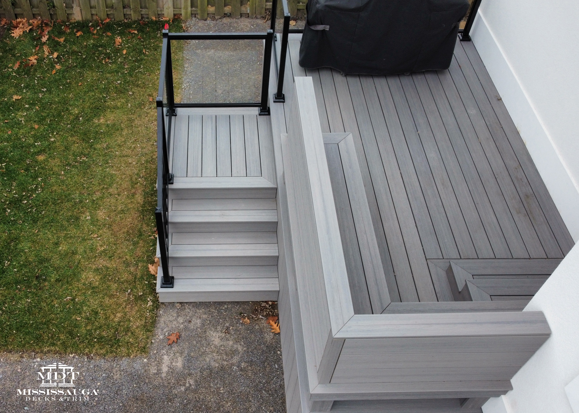 Small gray accessibility ramp with black handrails beside a raised gray deck and a porch bench