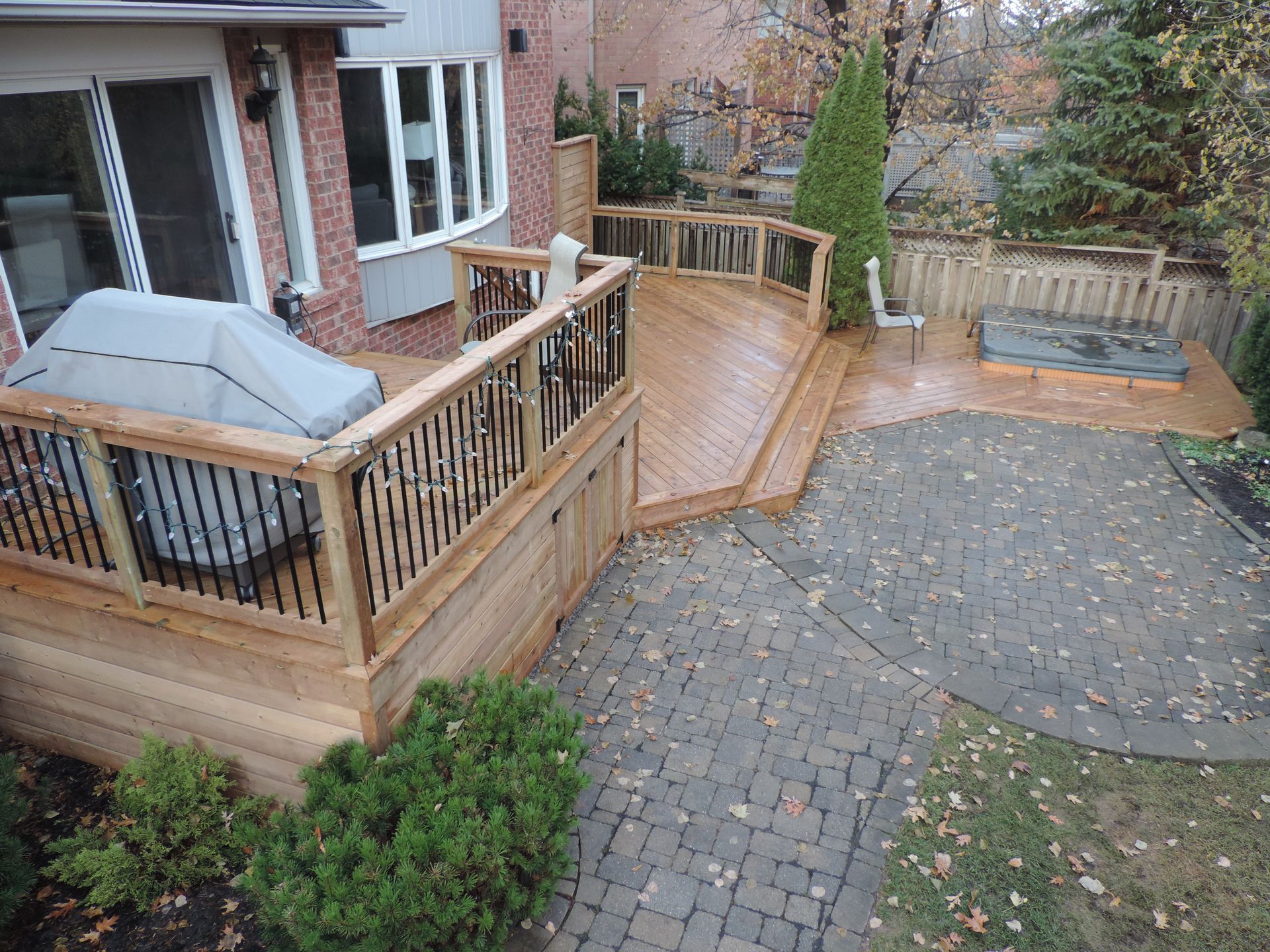 Backyard deck with hot tub, curved wooden ramp, and stone patio beside a house