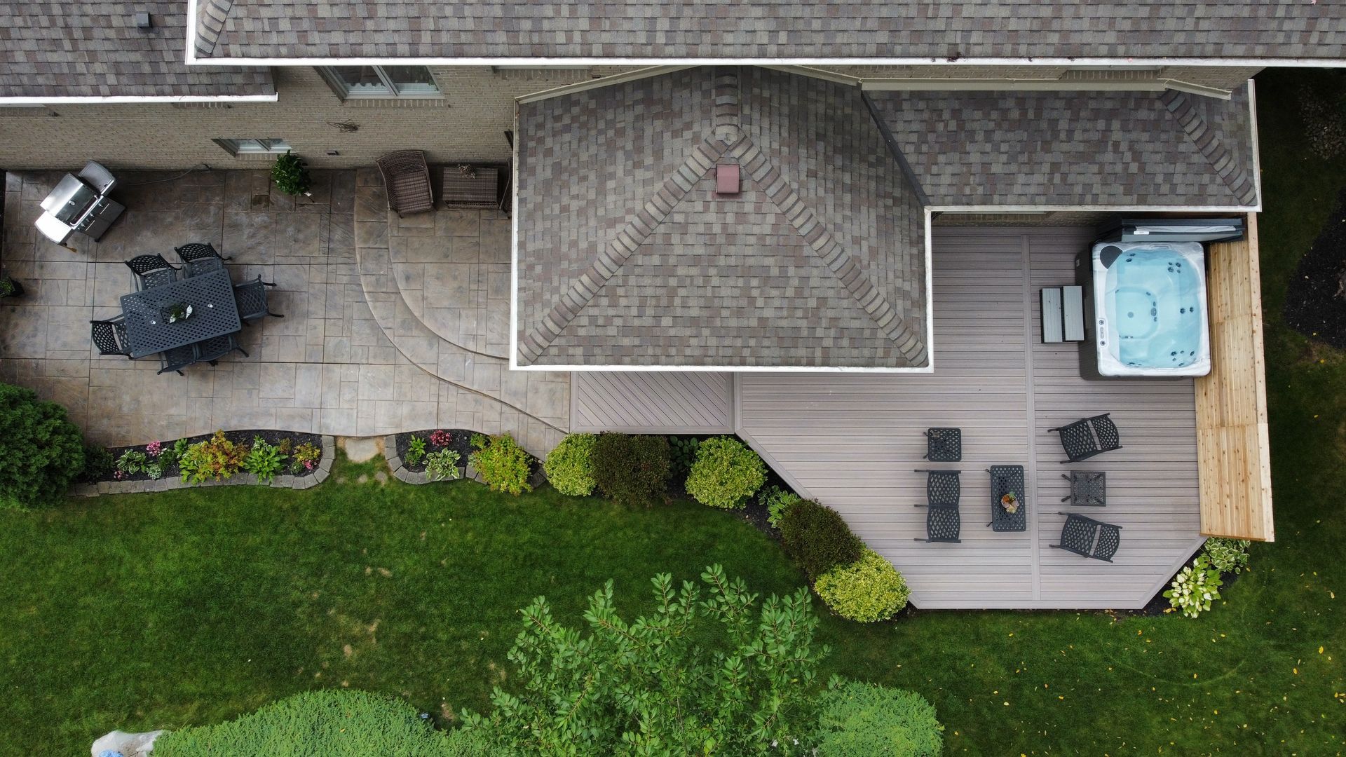 Aerial view of a backyard patio with outdoor furniture, a hot tub, and a grassy lawn beside a house.