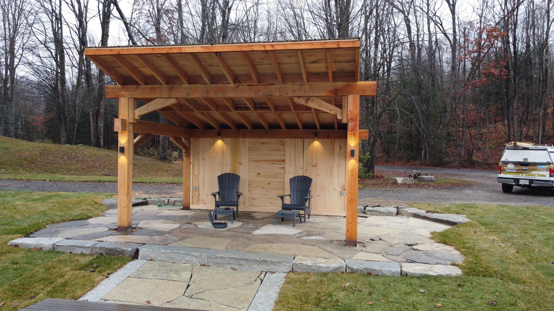 Covered patio with two chairs and warm string lights in a wooded yard at dusk