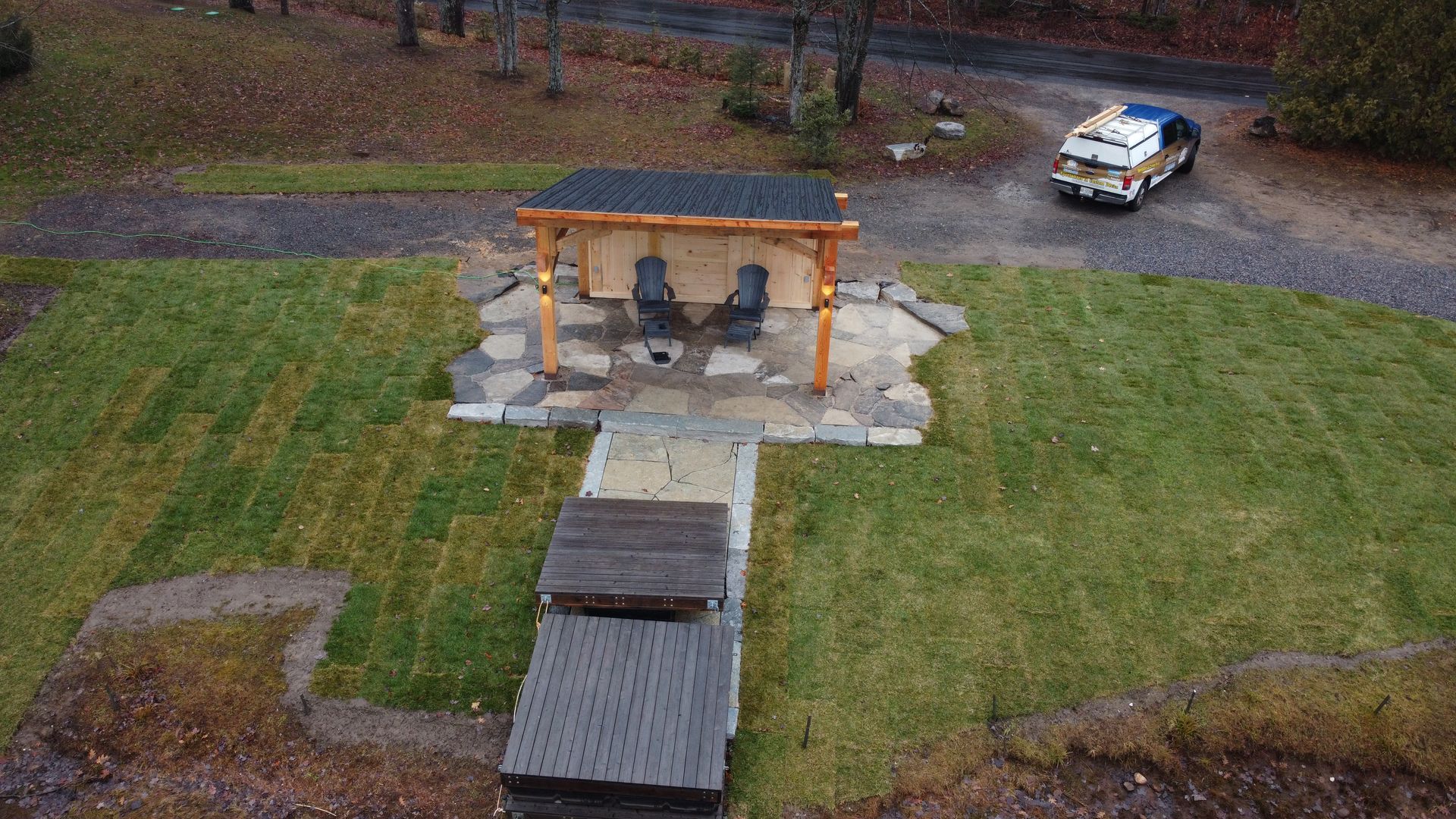 Aerial view of a stone pavilion and walkway in a grassy park, with a white truck parked nearby.