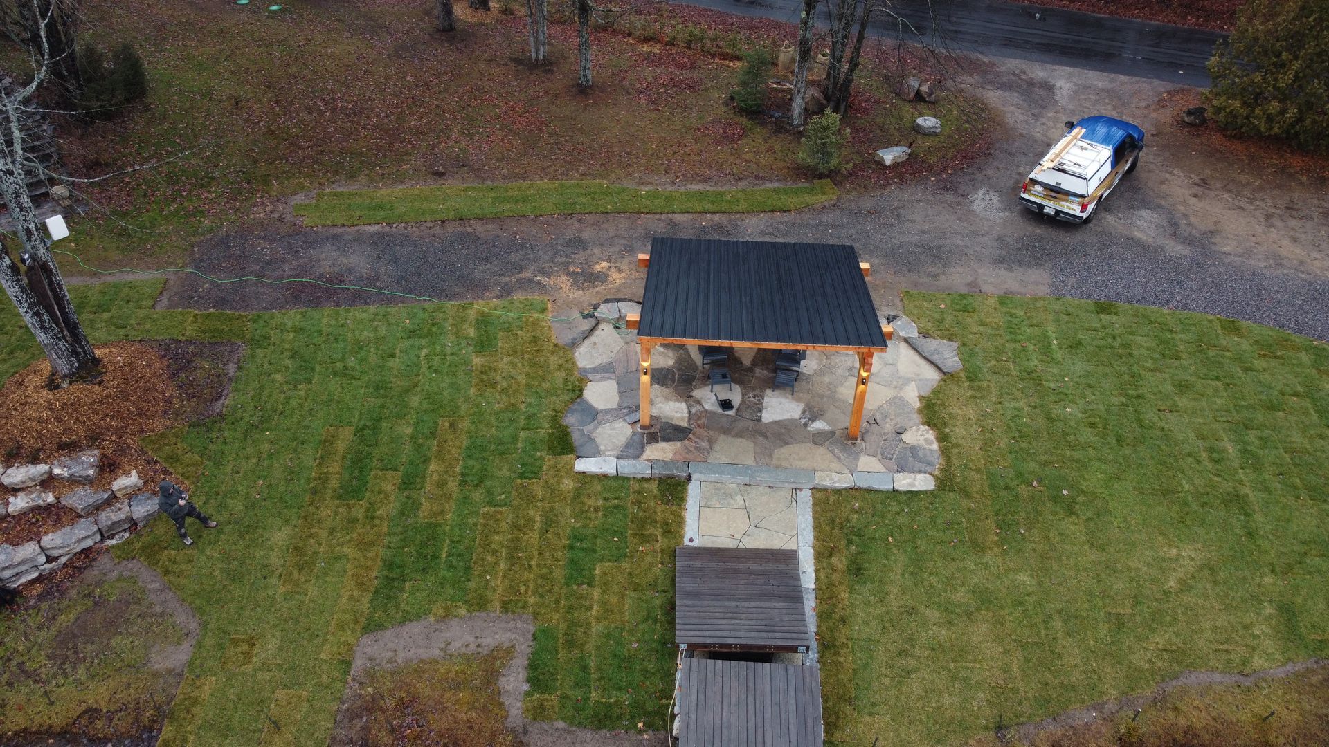 Overhead view of a small gazebo with a picnic table in a grassy park, with a white vehicle nearby