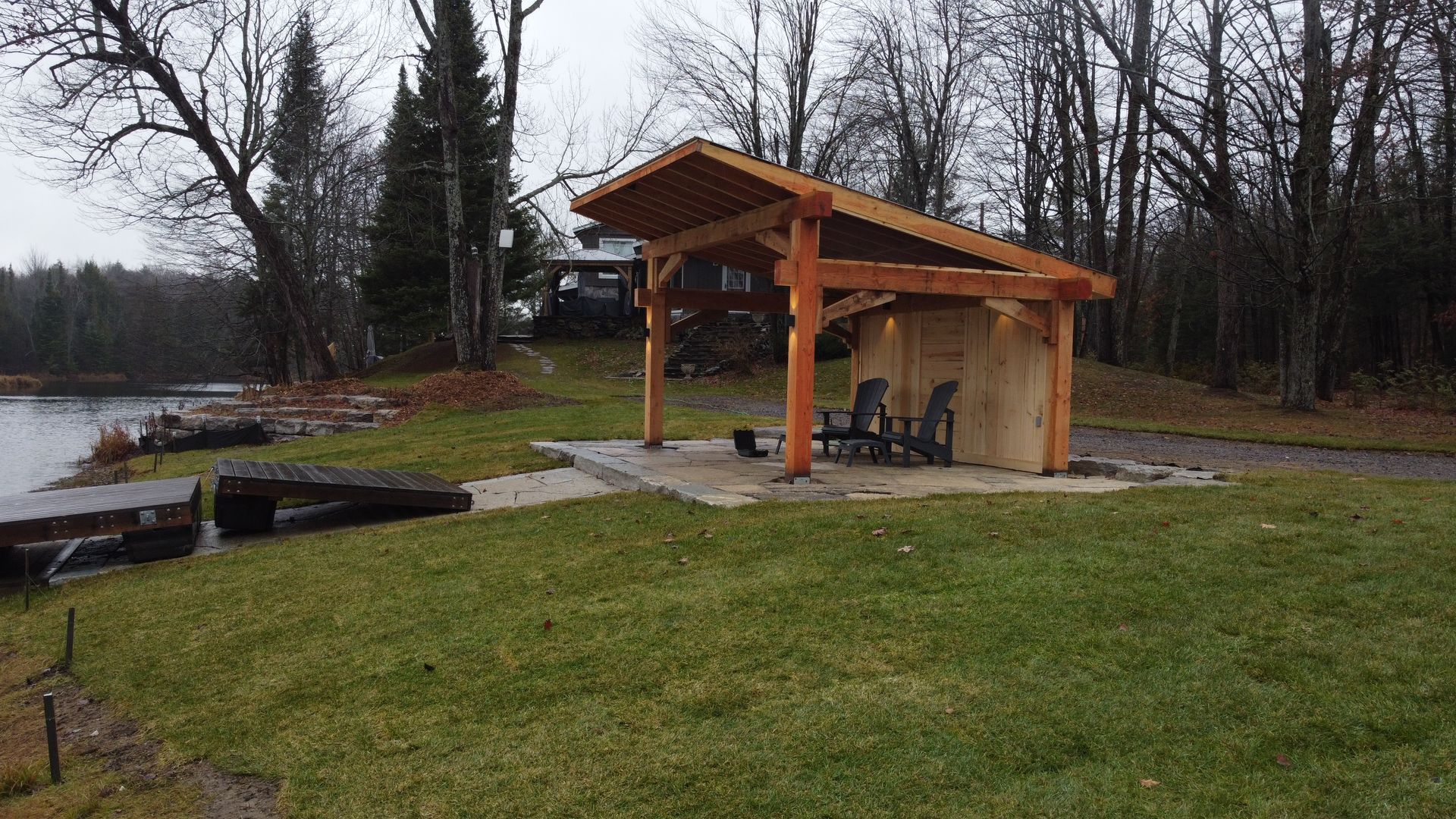 Covered picnic shelter by a lakeside, with benches and a grassy park area on a cloudy day