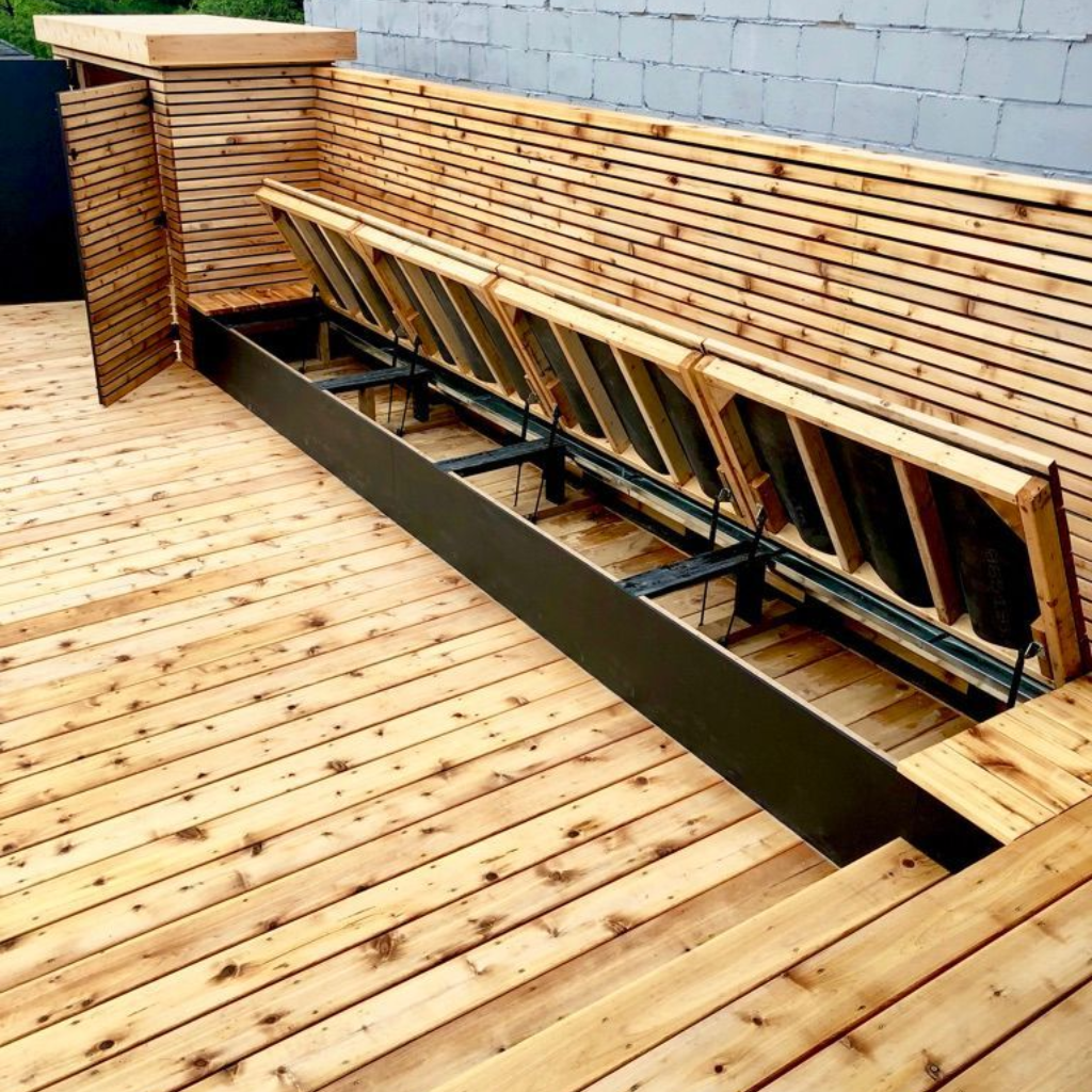 Wooden deck with a long slatted bench built into a recessed black metal frame beside a gray wall