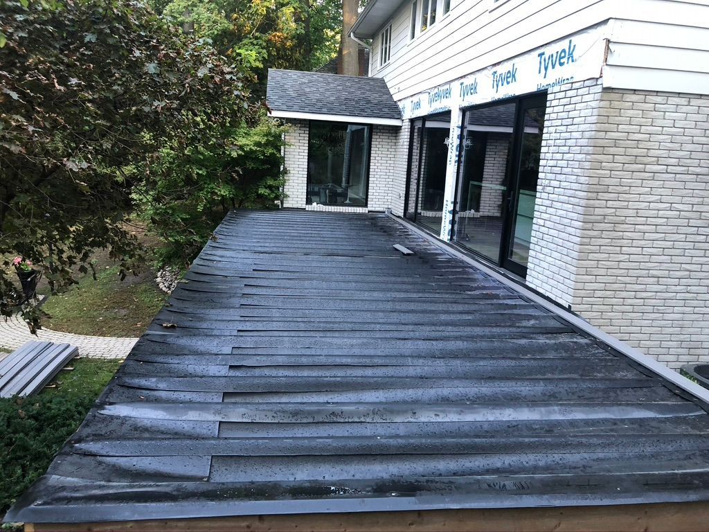 A flat roof on a building with water droplets. Next to windows with dark frames, and a brick wall.