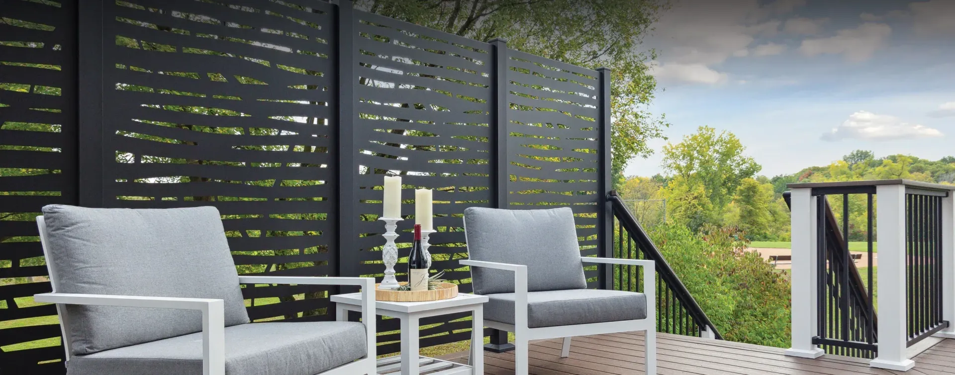 Outdoor patio with black privacy fence, white furniture, candles, and a scenic view.