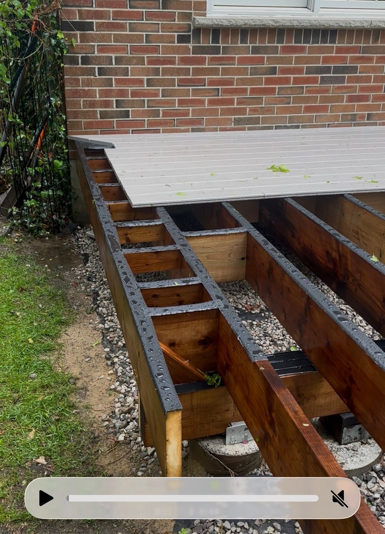 Deck construction: Brown composite decking being installed on wooden frame in a backyard.