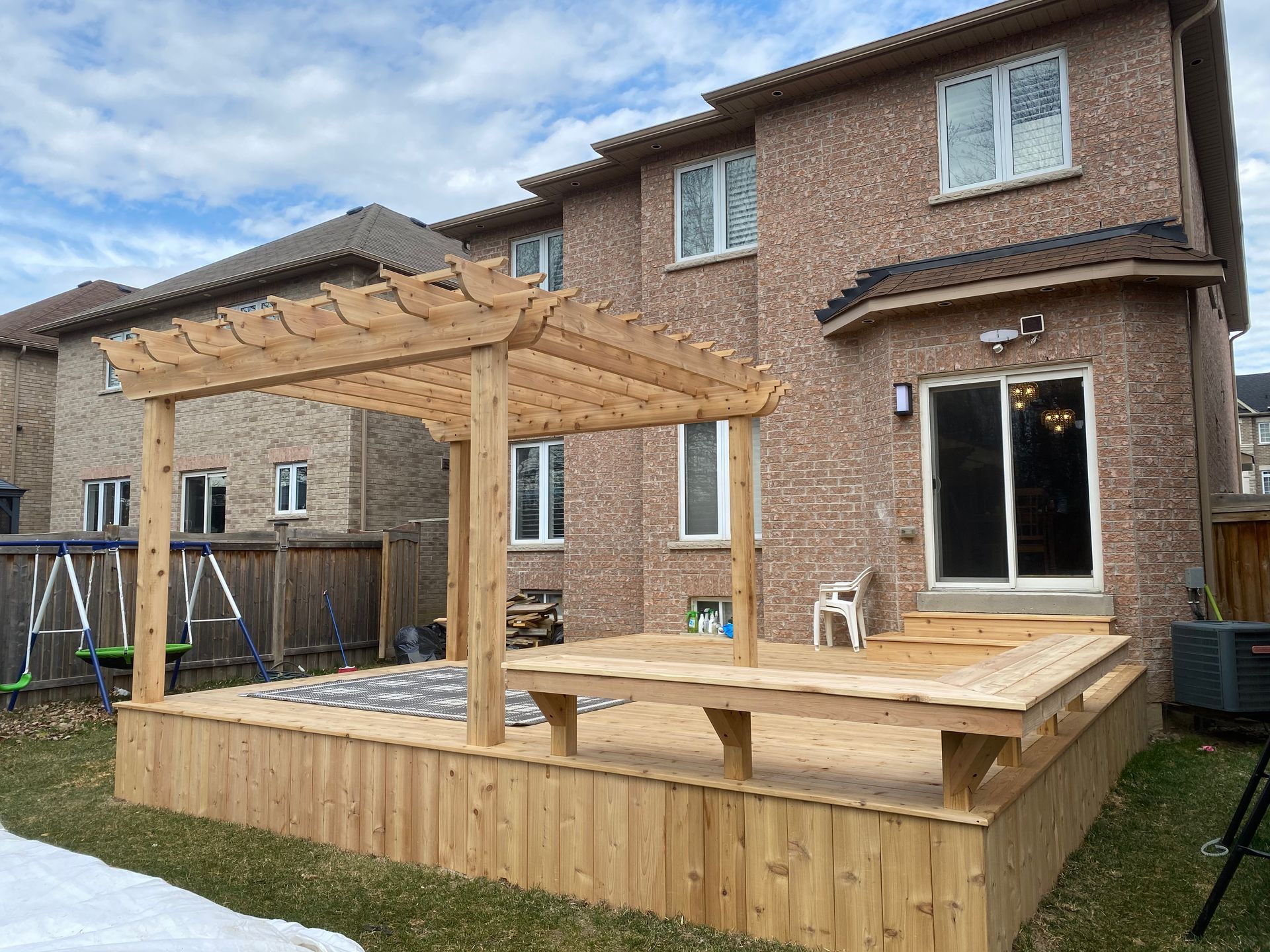 A wooden deck with a pergola in the backyard of a house.