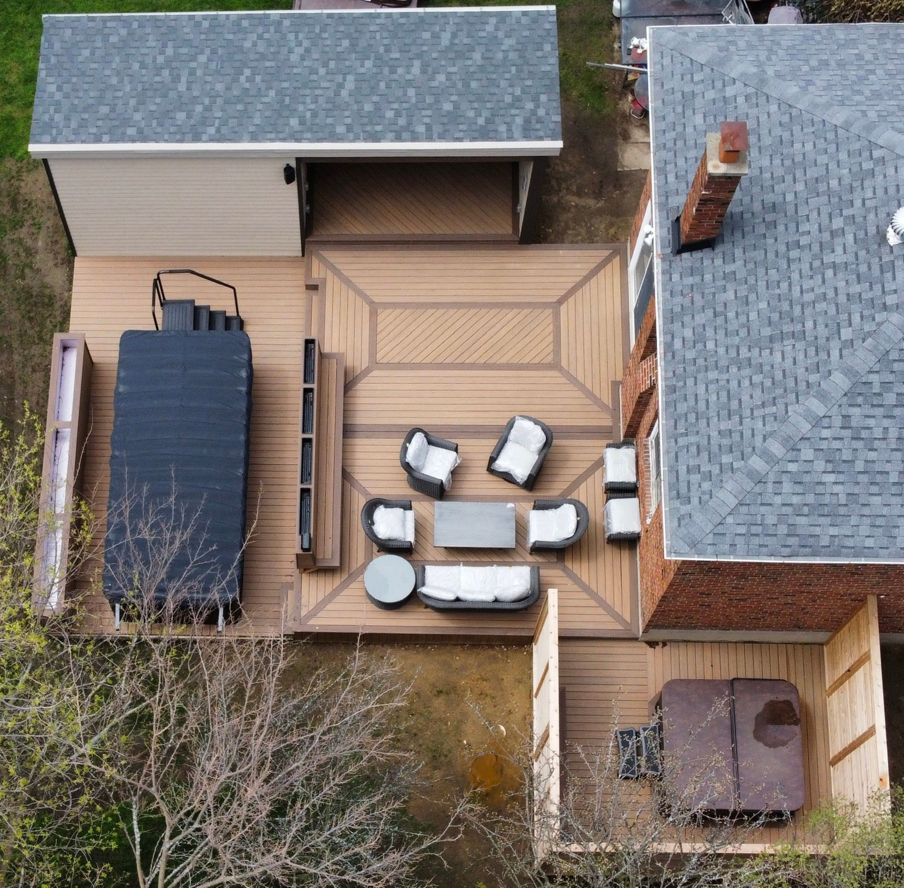 Aerial view of a backyard deck with outdoor seating, a grill, and adjacent sheds beside a house.