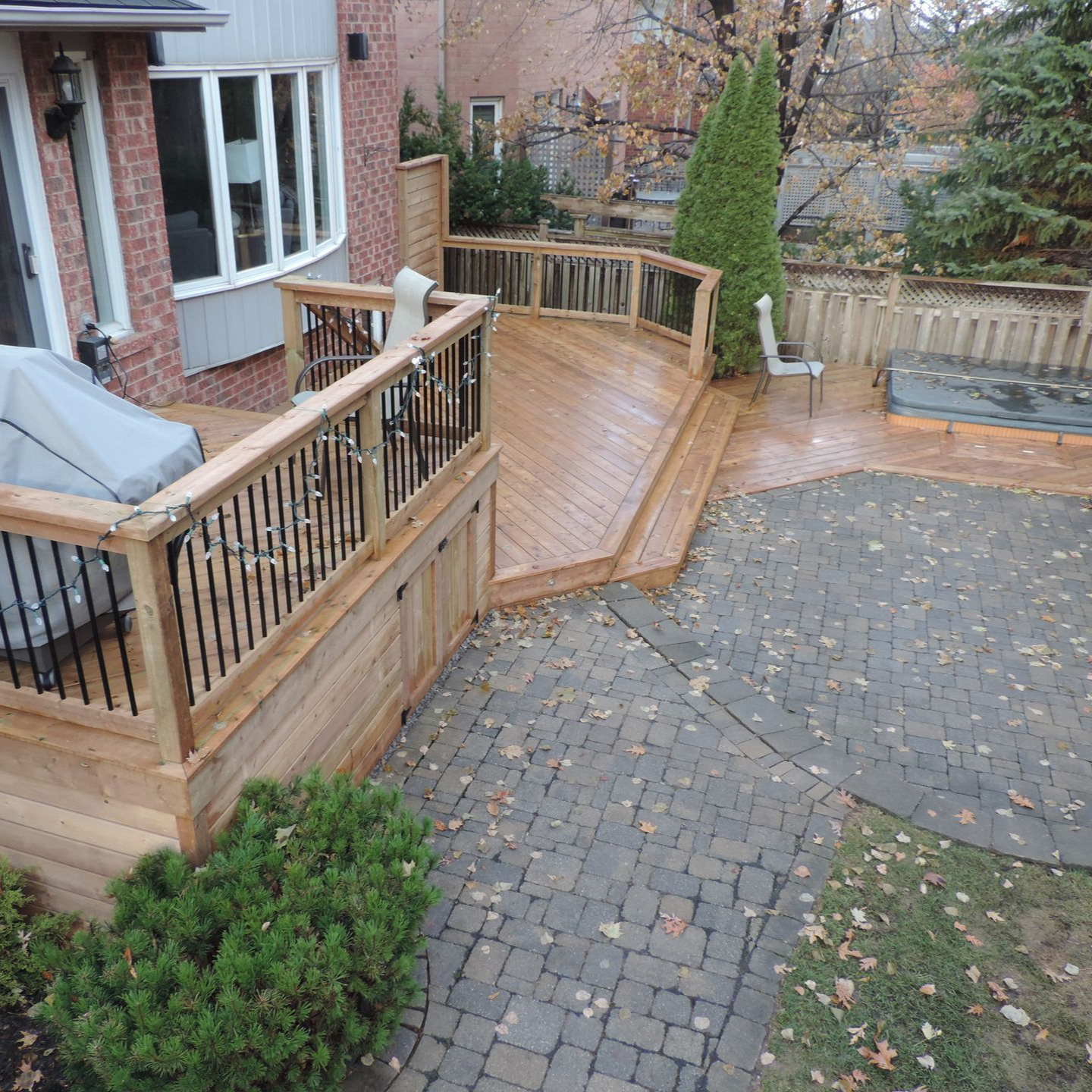 Backyard deck with hot tub, curved wooden railing, stone patio, and gravel path beside a house