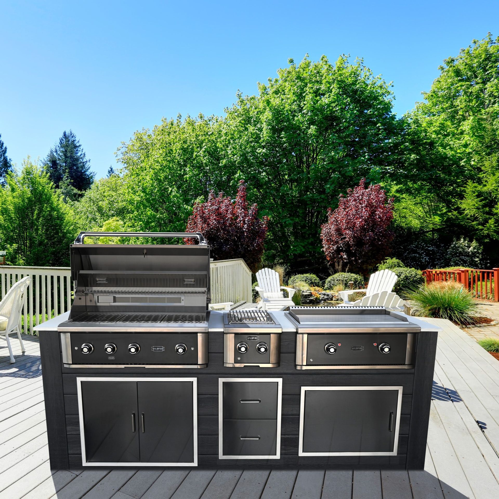 Outdoor stainless steel grill island on a sunny patio with chairs and trees in the background