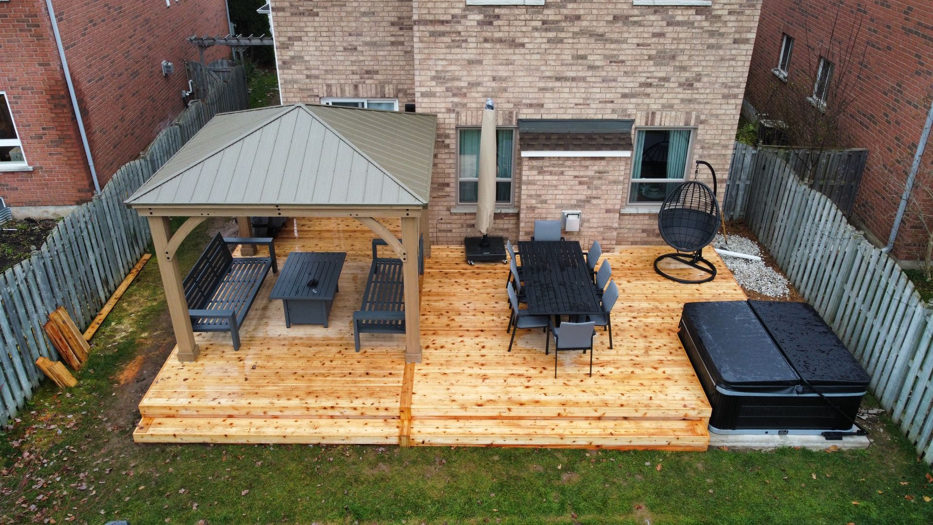 An aerial view of a backyard with a wooden deck , gazebo , table and chairs.