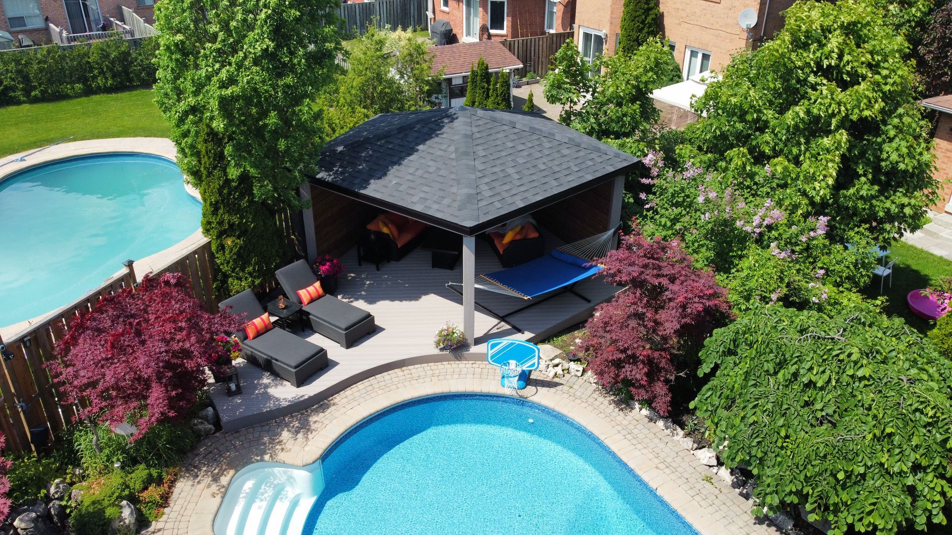 Apartment pool area with two blue pools, a shaded gazebo, and lounge chairs surrounded by greenery
