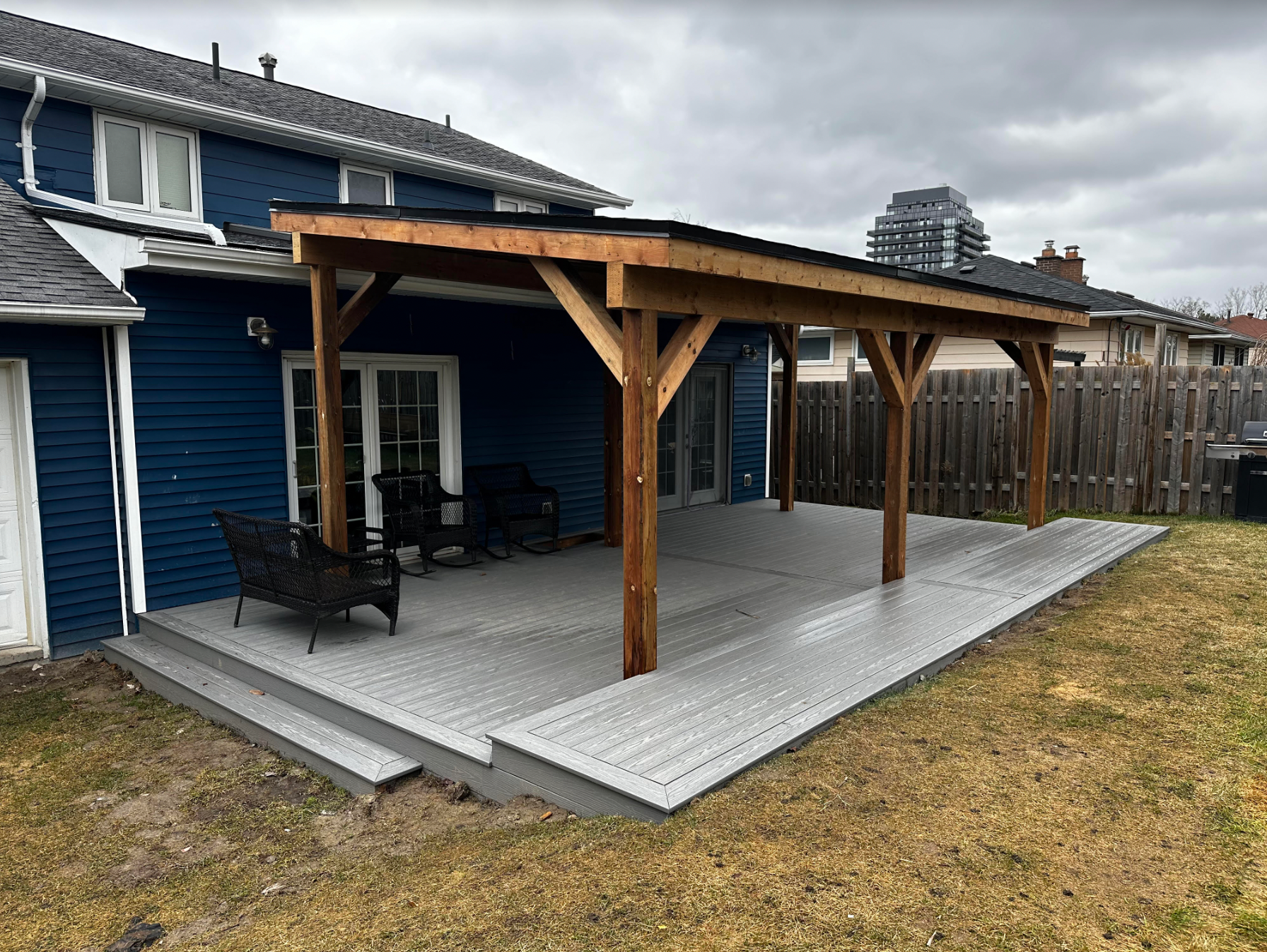 Wooden patio deck with pergola attached to a blue house, featuring outdoor seating.