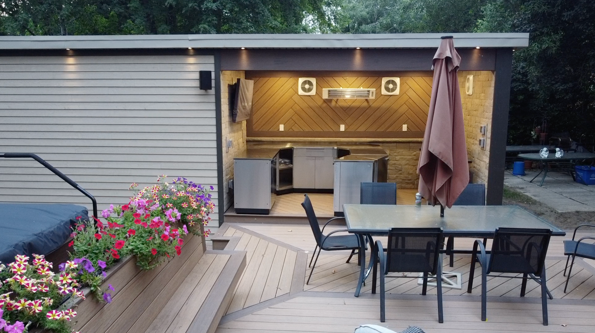 Modern backyard patio with dining table, umbrella, flower boxes, and open sliding doors into a lit seating area