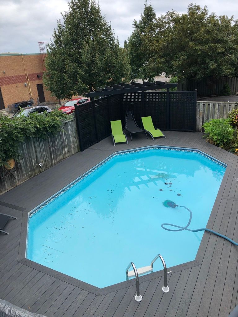 Backyard pool with two green loungers, black fence, and surrounding deck boards