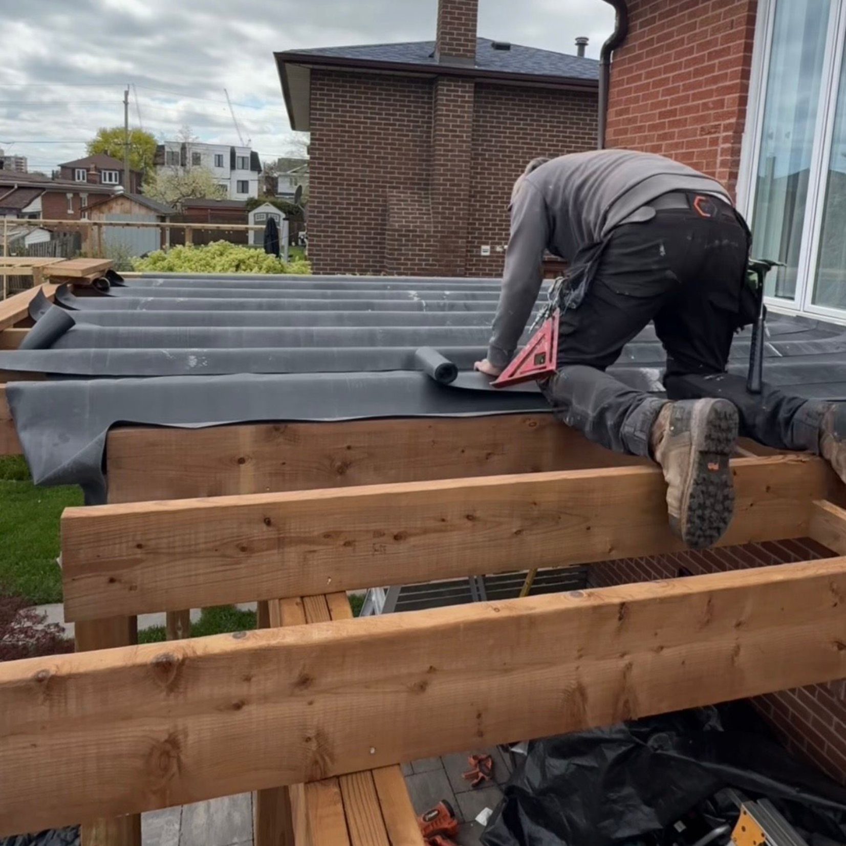 Worker installing roofing membrane on a flat roof beside a brick house