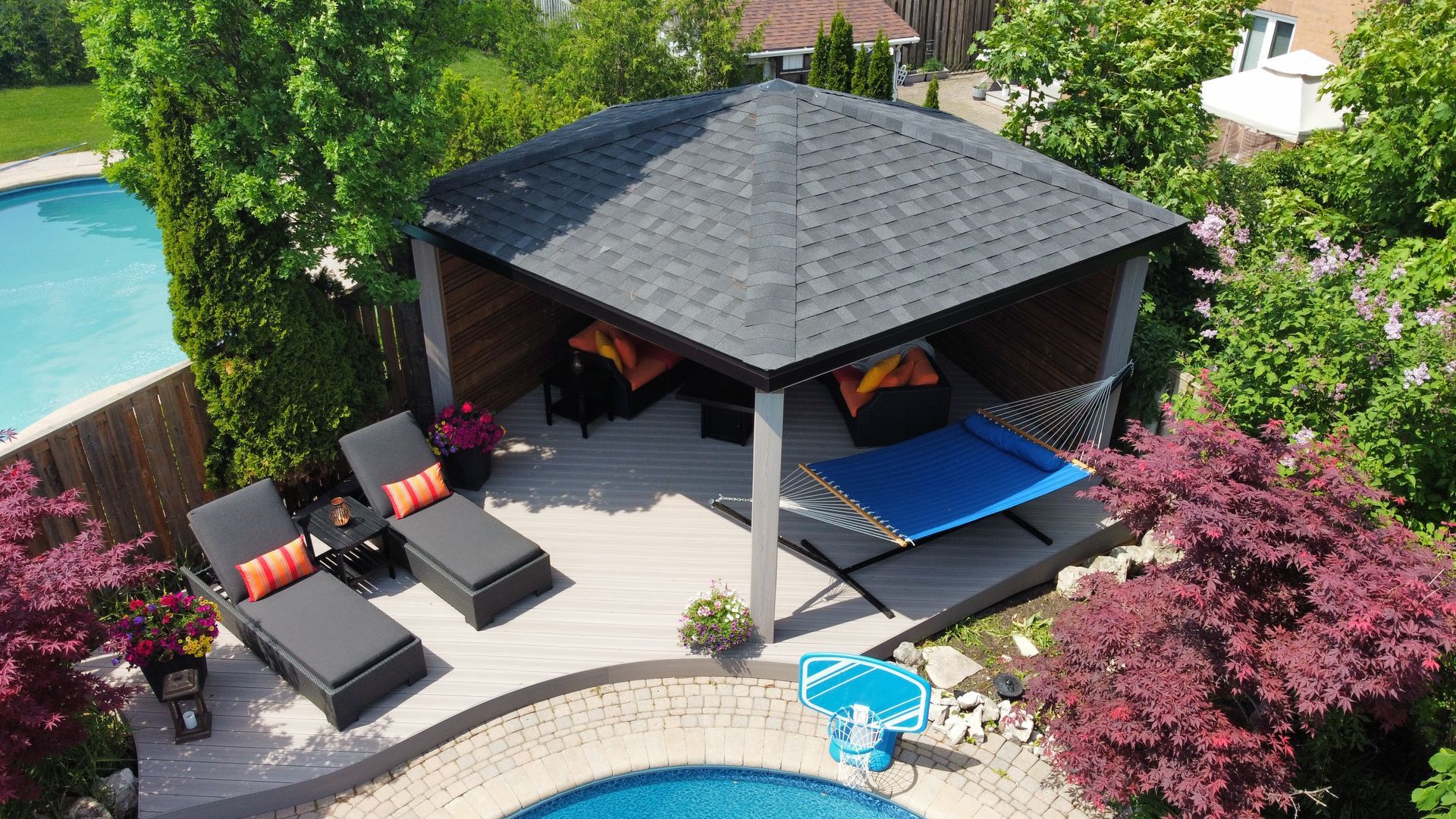 Backyard patio cabana with lounge chairs, blue canopy, and a swimming pool surrounded by greenery
