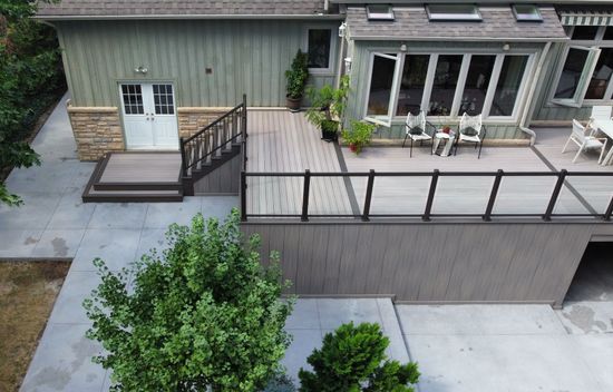 Backyard patio with gray concrete, dark railing, steps, and a house exterior with windows and a door
