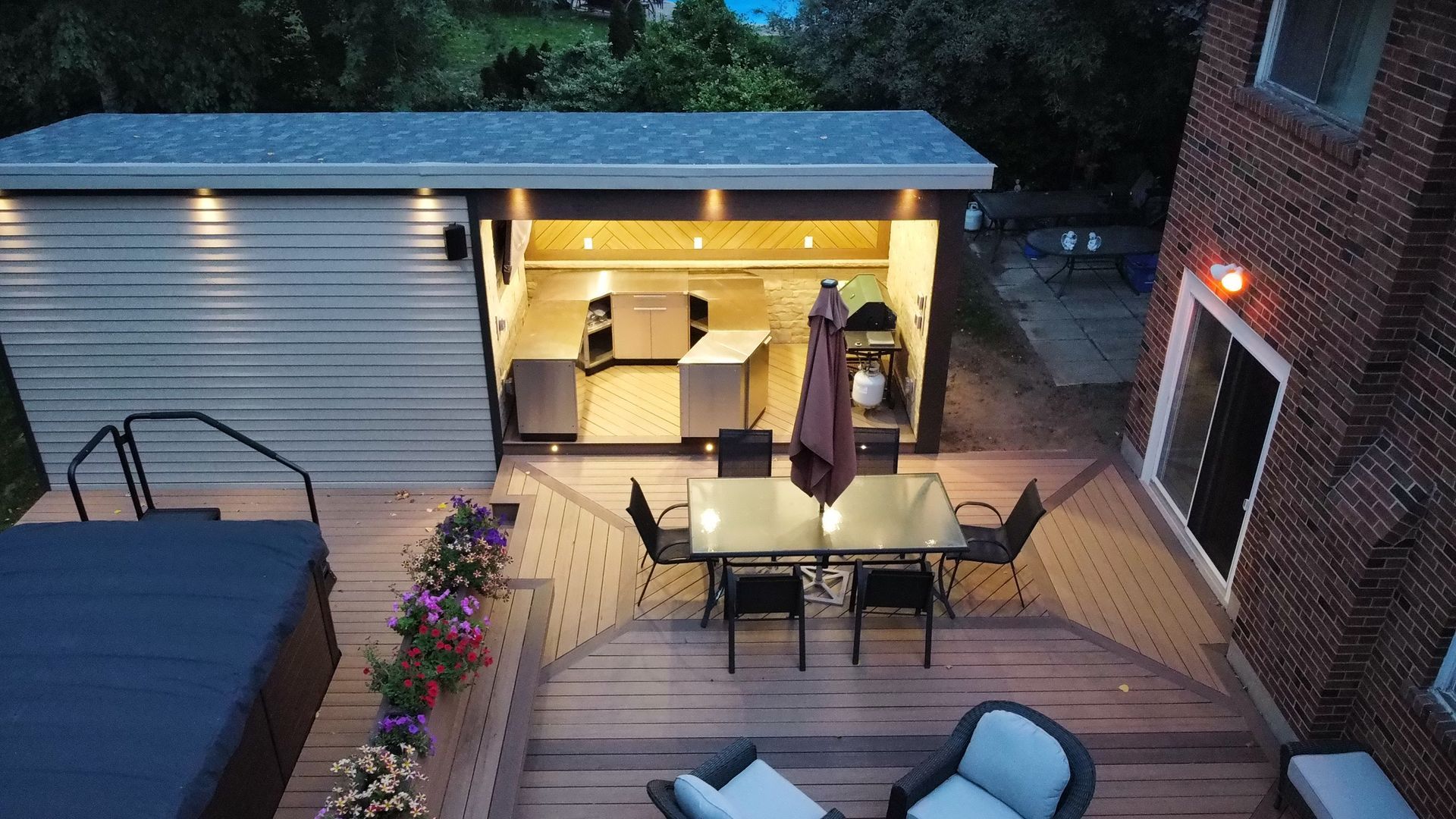 Backyard deck at dusk with outdoor dining table, sofa seating, and lit patio area near a garage
