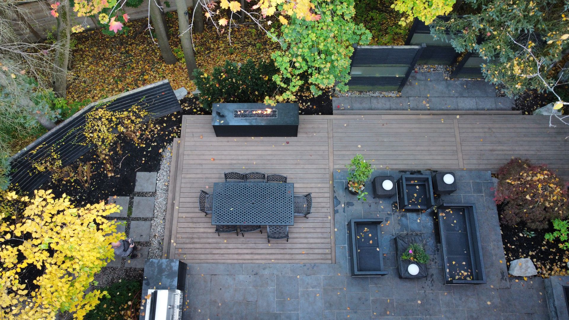 Overhead view of a wooden patio with black outdoor furniture and surrounding garden plants