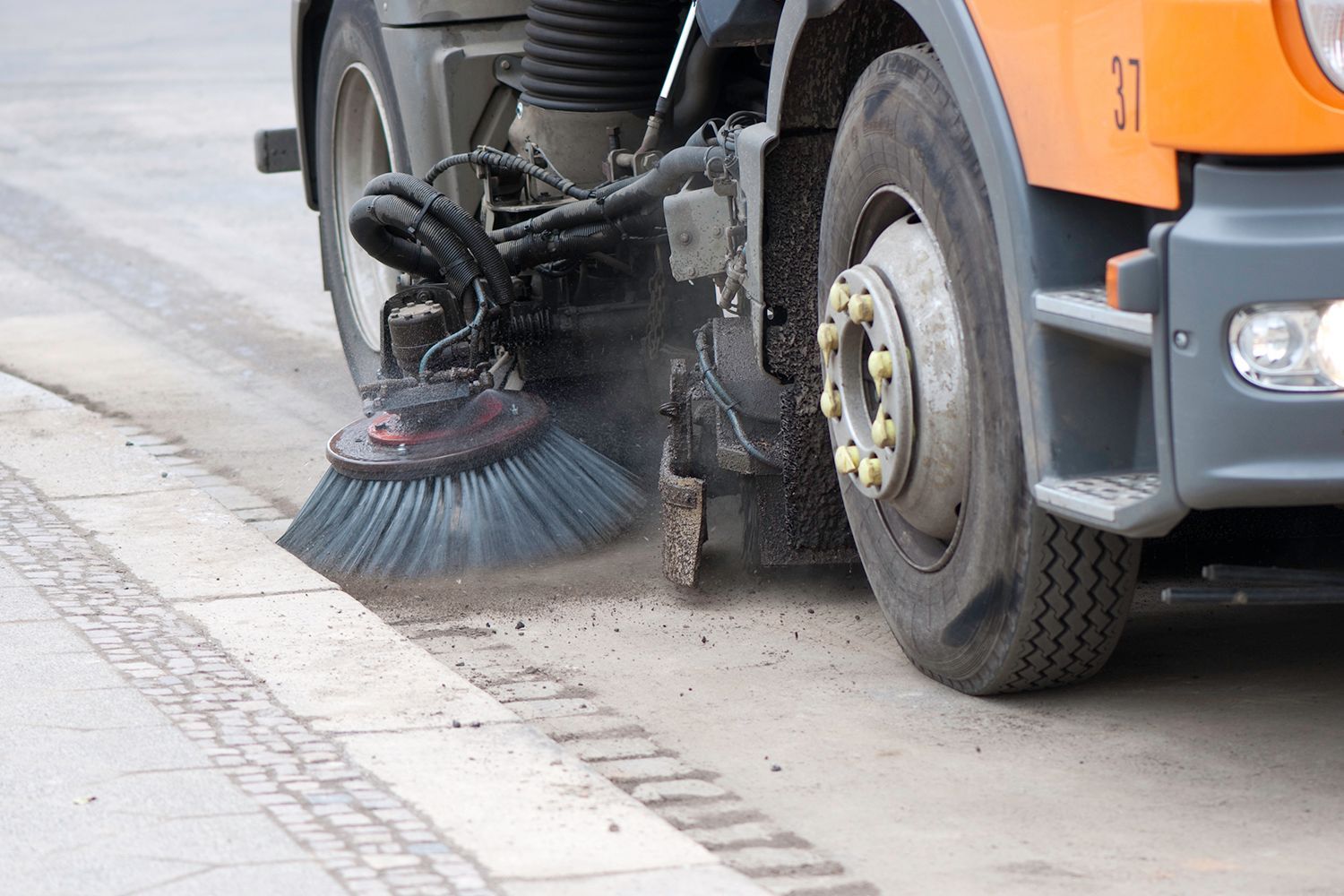Street sweeper cleaning a sidewalk. Orange truck with large brush sweeping dirt.