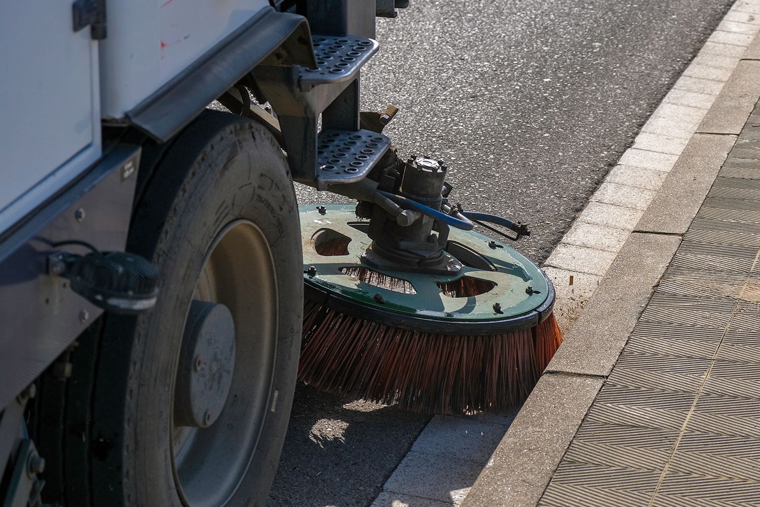 Street sweeper cleaning a sidewalk, showing the brush and wheel.
